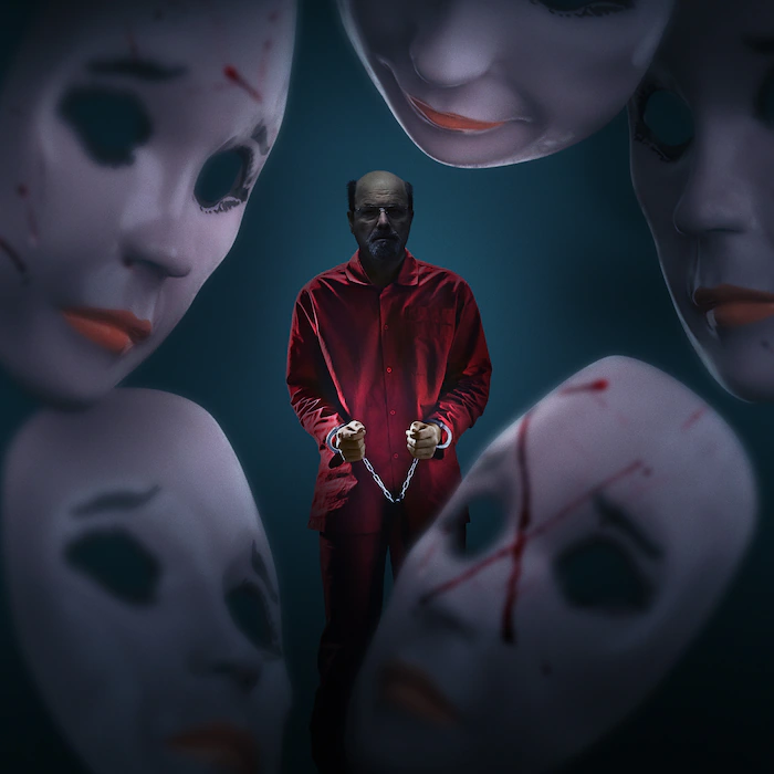 Dennis Rader algemado, vestindo macacão vermelho, cercado por grandes máscaras brancas com marcas de sangue.